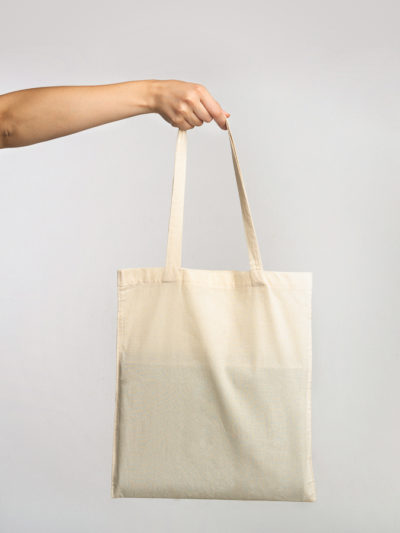 Female Hand Holding White Blank Eco Bag Over Gray Studio Background. Ecology And Minimalism Concept